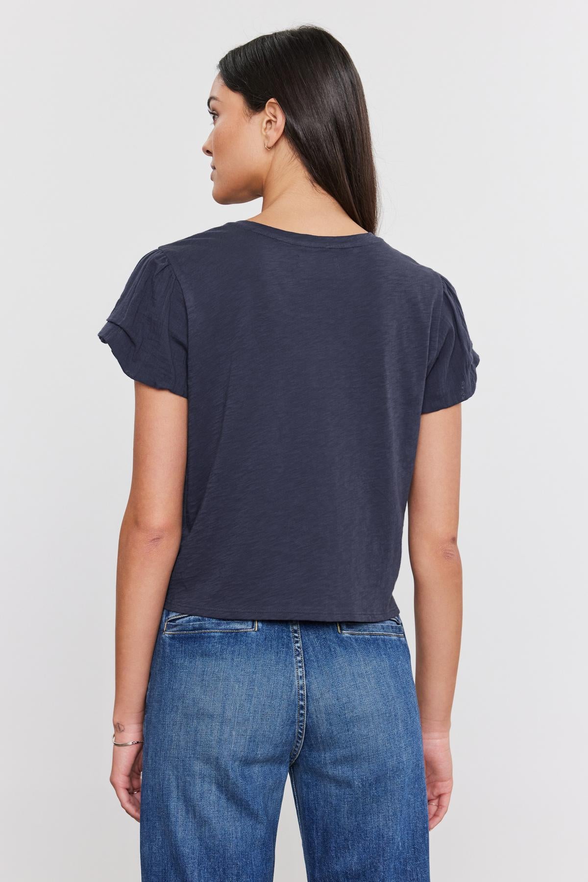 Woman viewed from behind, wearing a dark blue cotton slub DELLA TEE with pleated sleeve detail and blue jeans, standing against a white background. (Brand Name: Velvet by Graham & Spencer)-36805187338433