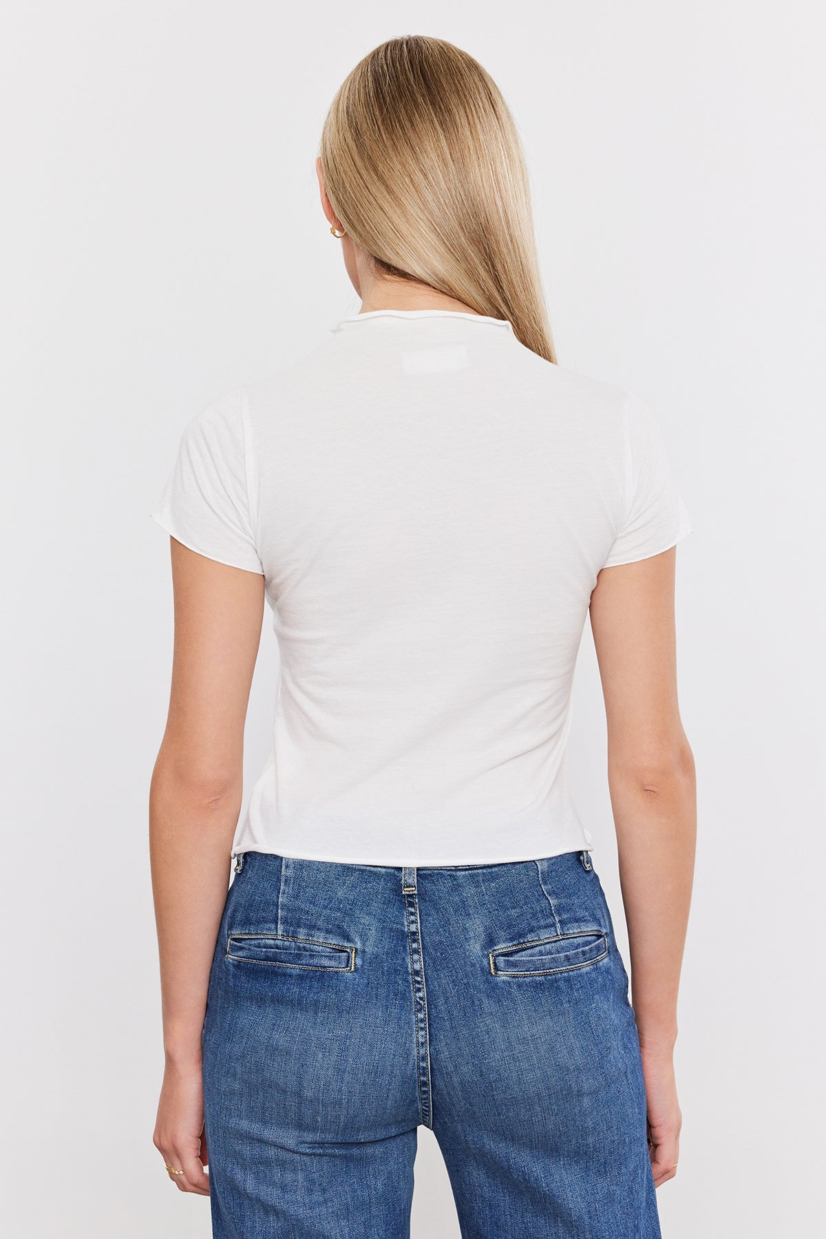 The back view of a woman wearing jeans and a white Velvet by Graham & Spencer Jackie Mock Neck Tee with a cropped silhouette.-35982216102081