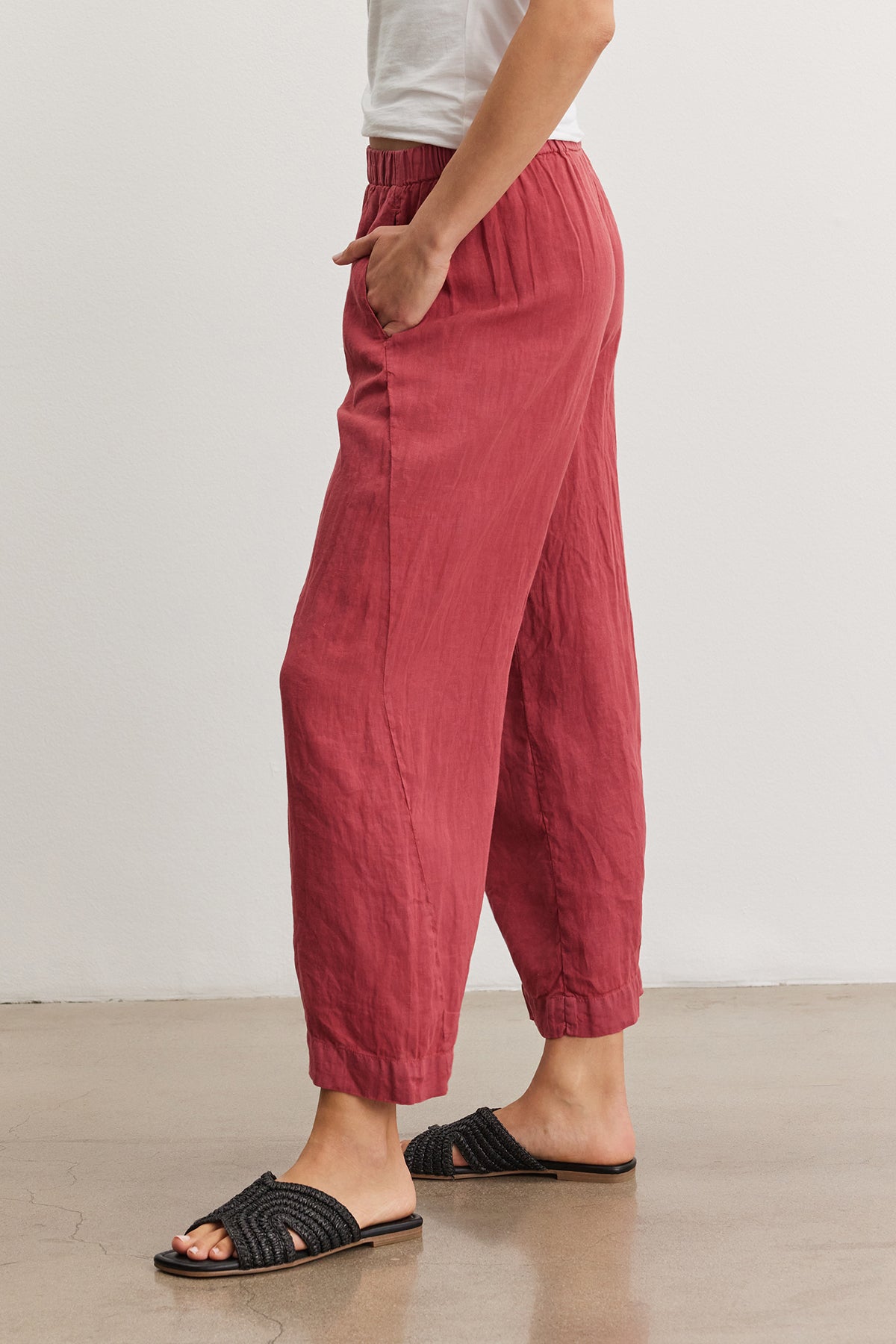 Side view of a person wearing red Velvet by Graham & Spencer LOLA LINEN PANT and black slide sandals on a neutral background.-36909573341377
