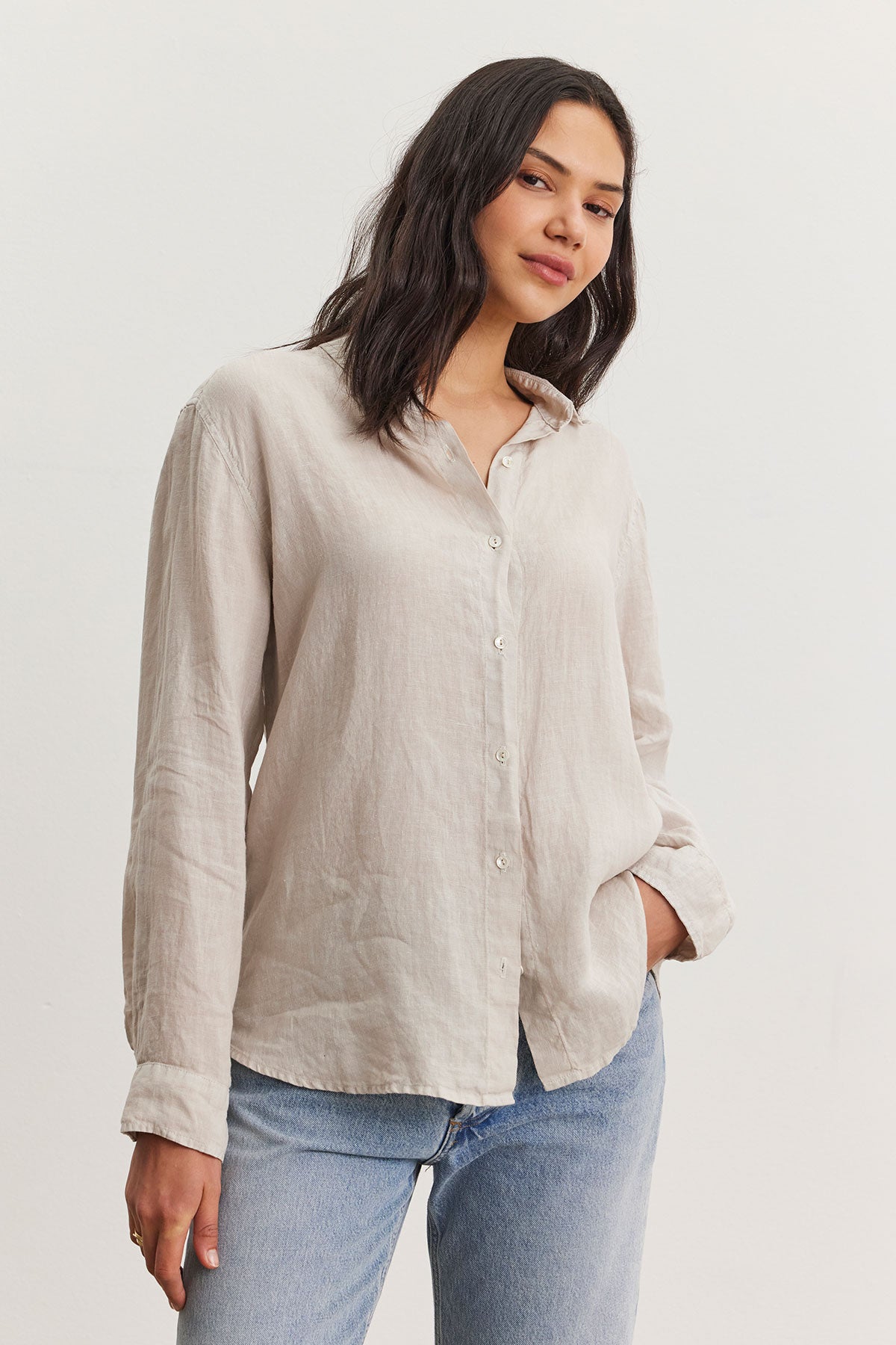 A woman wearing a Velvet by Graham & Spencer Willow Linen Button-Up Shirt paired with denim jeans stands confidently while slightly tilting her head, giving a relaxed pose in a bright indoor setting.-36998739067073