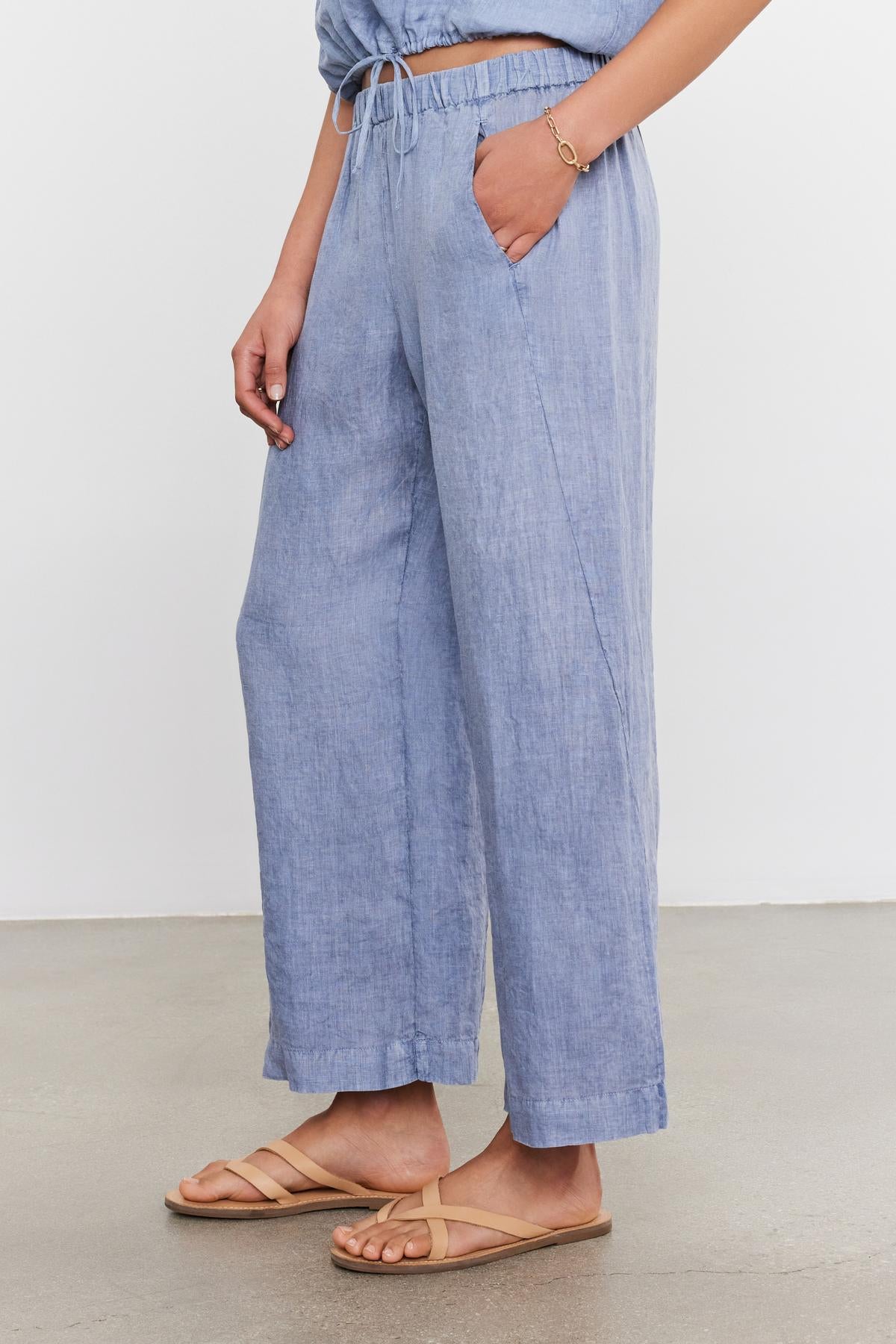 A person wearing Velvet by Graham & Spencer LOLA LINEN PANTS with an elastic waist and tan sandals, focusing on the lower half of the body.-36910133051585