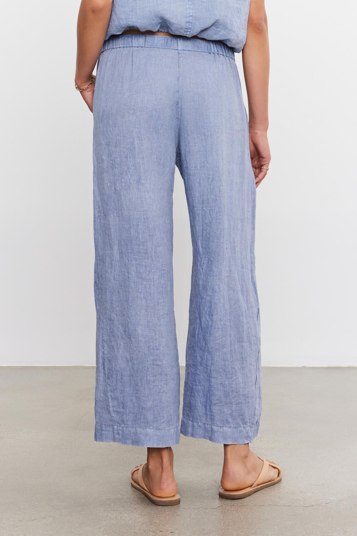 Woman standing in Velvet by Graham & Spencer's LOLA LINEN PANT ankle crop trousers and matching top, viewed from the back, with hands partially tucked in pockets.-36910133084353