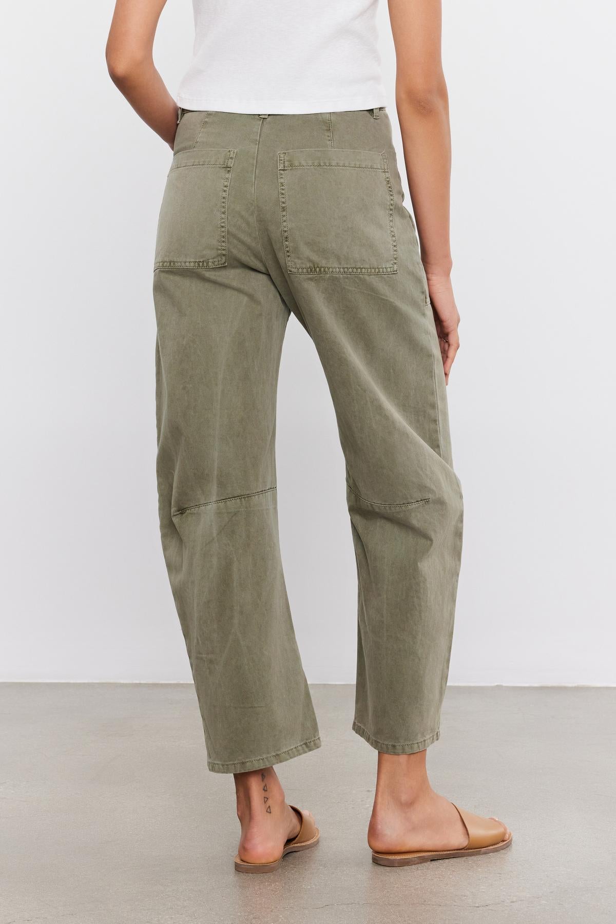 Rear view of a person wearing Velvet by Graham & Spencer BRYLIE SANDED TWILL UTILITY PANT trousers and a white t-shirt, standing on a grey floor with brown shoes.-37000518140097