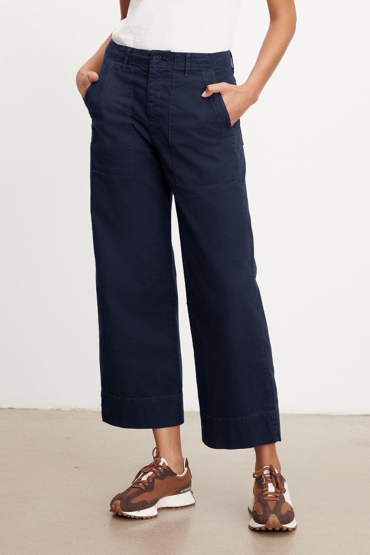 A person wearing navy blue Velvet by Graham & Spencer MYA COTTON CANVAS PANTS and a white shirt paired with brown and white sneakers, standing in a neutral pose against a plain background.-36999933886657