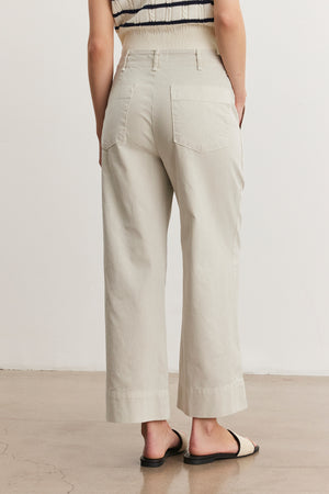 A person wearing beige Velvet by Graham & Spencer MYA COTTON CANVAS PANT with a flared leg and black flat shoes, viewed from behind.