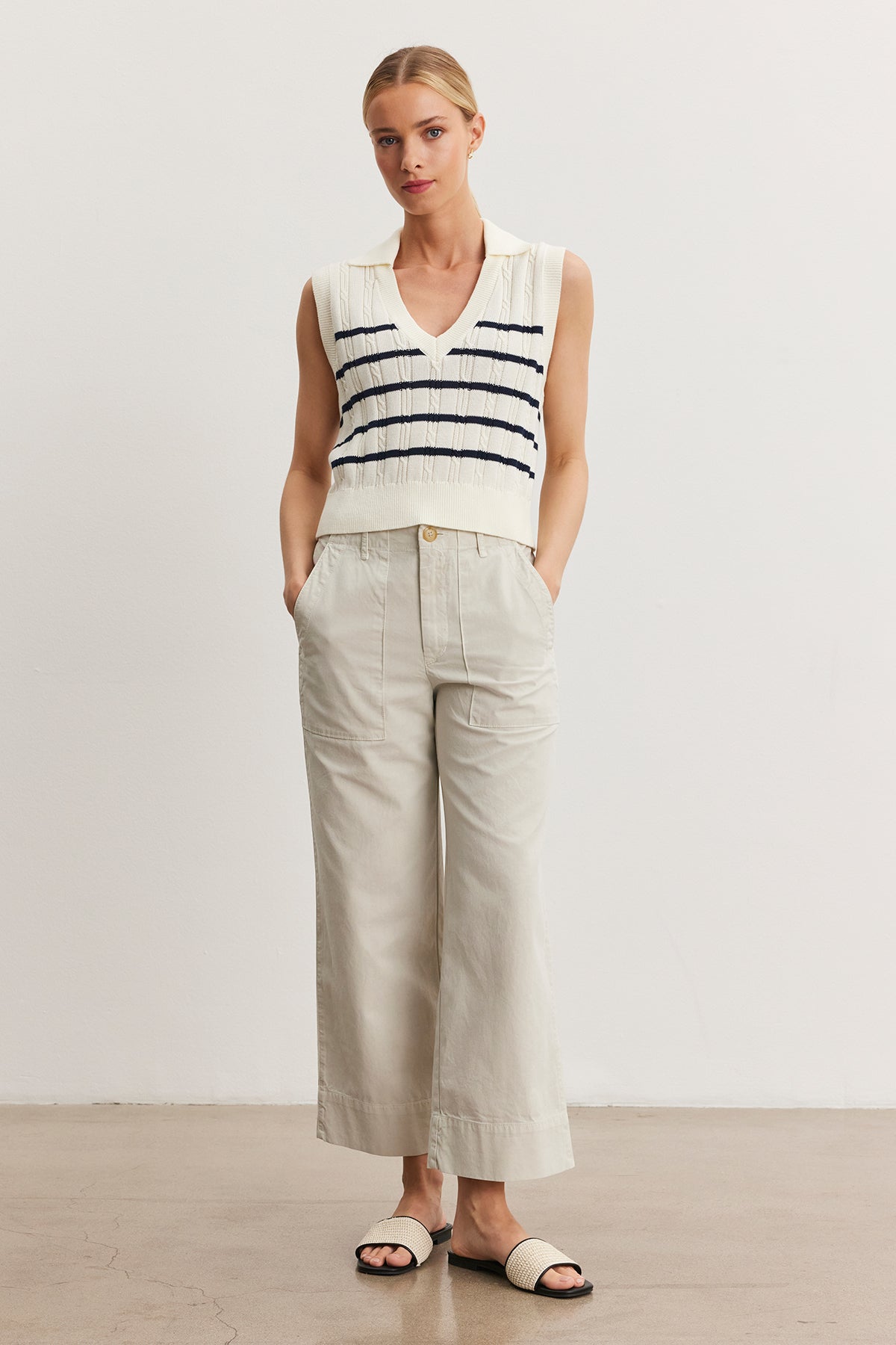Woman in a sleeveless white top with blue stripes and light beige Velvet by Graham & Spencer MYA COTTON CANVAS PANT, standing in a studio, wearing black sandals.-36998760726721
