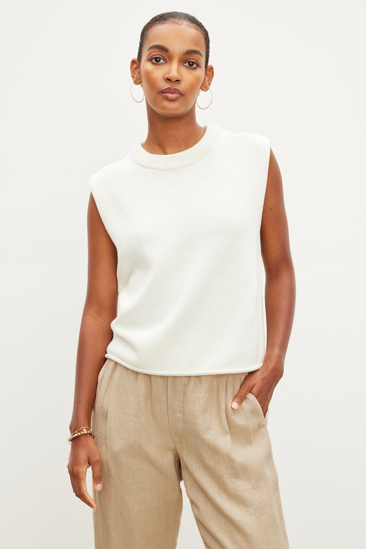 The model is wearing a white sleeveless ASTER CREW NECK SWEATER made from a luxurious cotton cashmere blend by Velvet by Graham & Spencer.-35955418464449