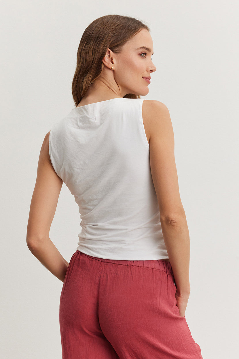 A woman in a Velvet by Graham & Spencer EMILIA TANK TOP and red pants, viewed from behind, looking over her shoulder with a neutral expression.