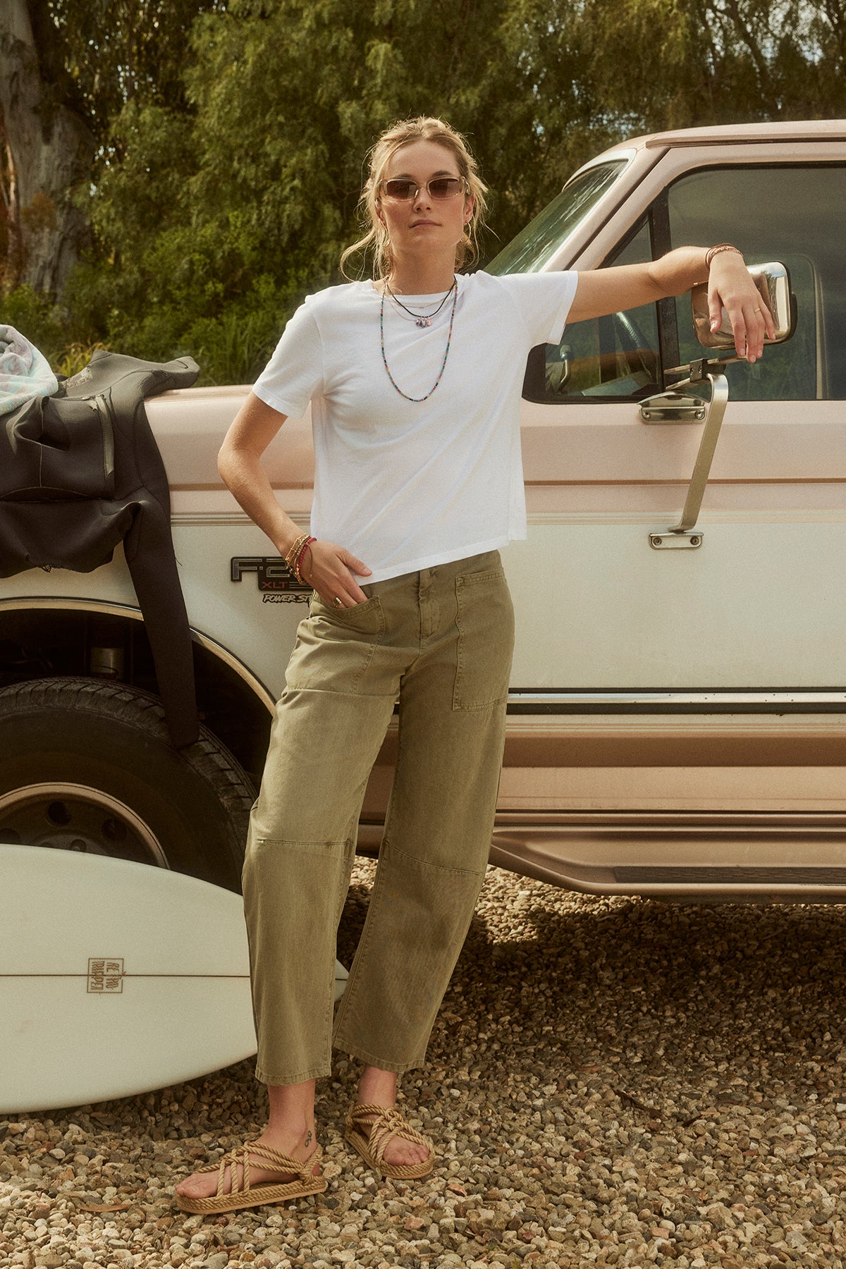 Woman in sunglasses, white t-shirt, and Velvet by Graham & Spencer BRYLIE SANDED TWILL UTILITY PANT leaning on a vintage pickup truck in a gravel area.-37000531476673