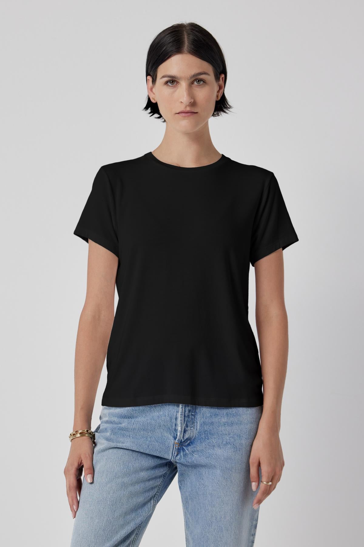 Woman in a classic Velvet by Jenny Graham SOLANA TEE and blue jeans standing against a plain background.-36463663972545