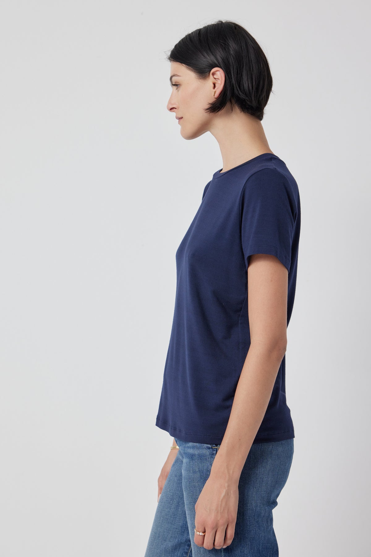 Profile view of a woman wearing a navy blue Velvet by Jenny Graham Solana Tee and jeans against a white background.-36463663874241