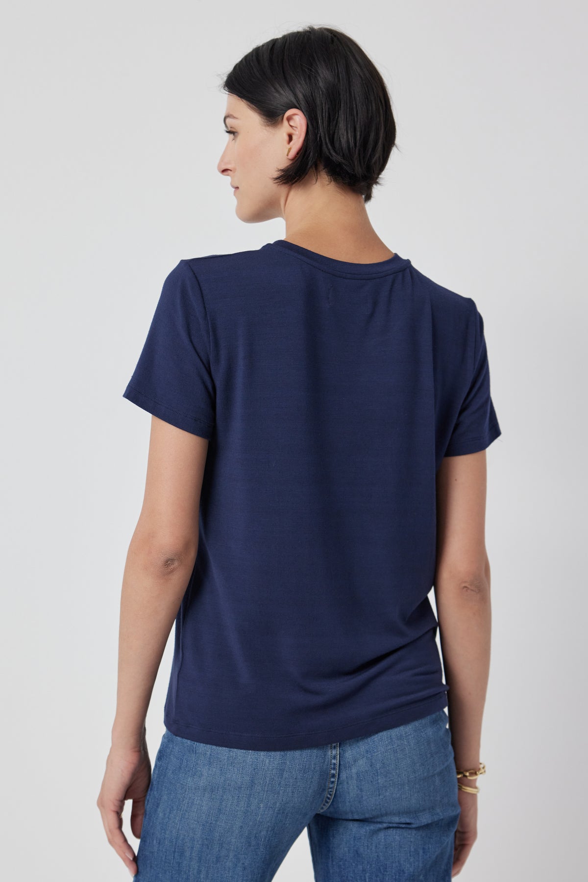 Woman posing with her back turned to the camera, wearing a navy blue Velvet by Jenny Graham SOLANA TEE and jeans.-36463663907009