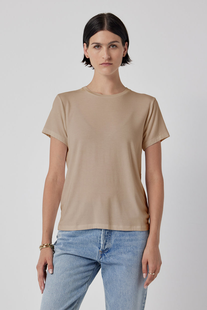 Woman modeling a classic Solana Tee by Velvet by Jenny Graham in beige and blue jeans against a white background.