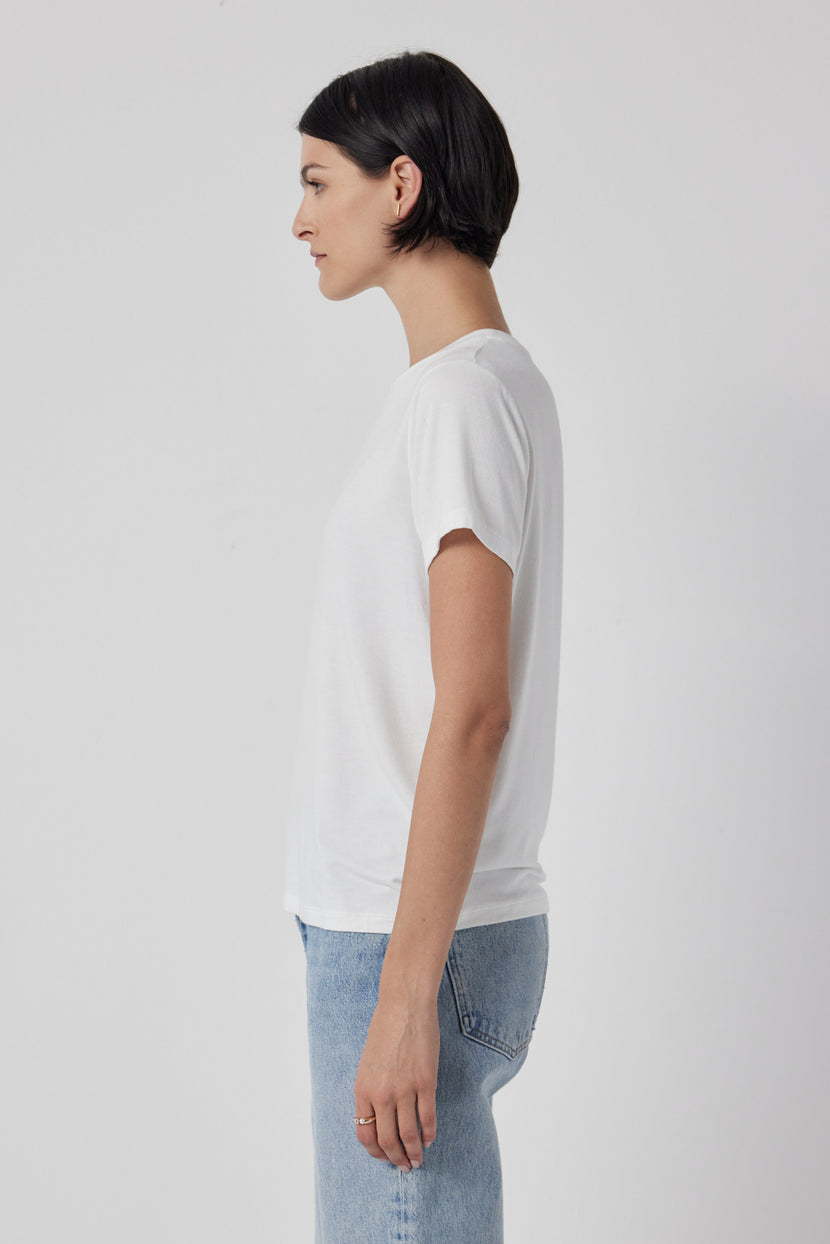 The woman is wearing a white Solana Tee by Velvet by Jenny Graham and jeans.