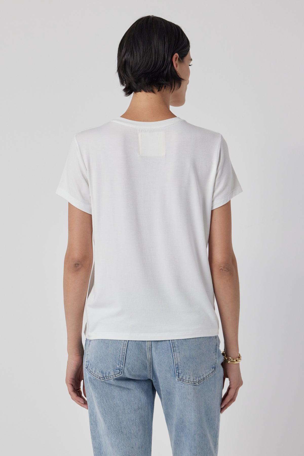 The woman is wearing a white Velvet by Jenny Graham SOLANA TEE and jeans, showing off the shrunken sleeve.-36002416787649