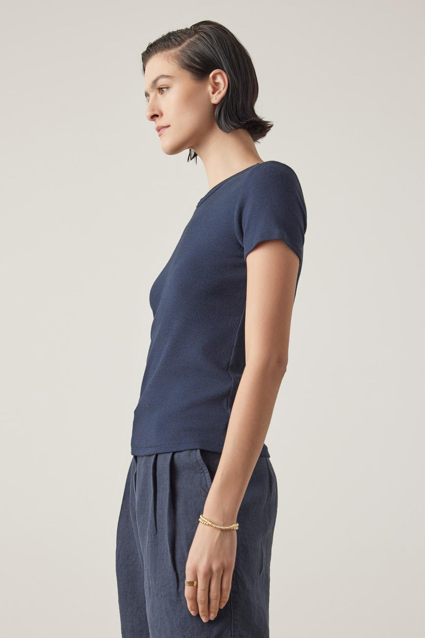 Woman in a BEDFORD TEE by Velvet by Jenny Graham, with a crew neckline and gray trousers, standing profile to the camera with focused expression, on a light background.