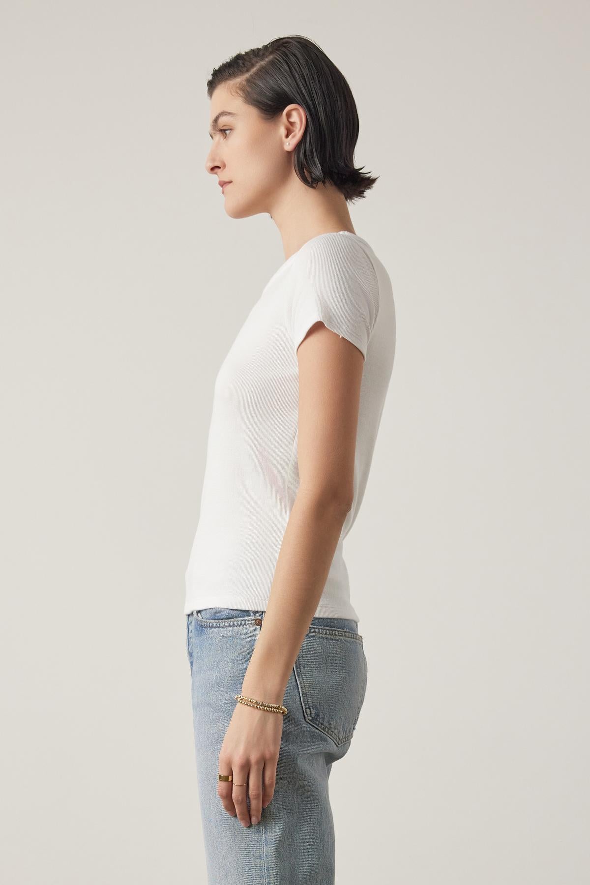 Side profile of a woman with short hair wearing a white BEDFORD TEE by Velvet by Jenny Graham with a crew neckline and jeans, standing against a light backdrop.-36753616797889