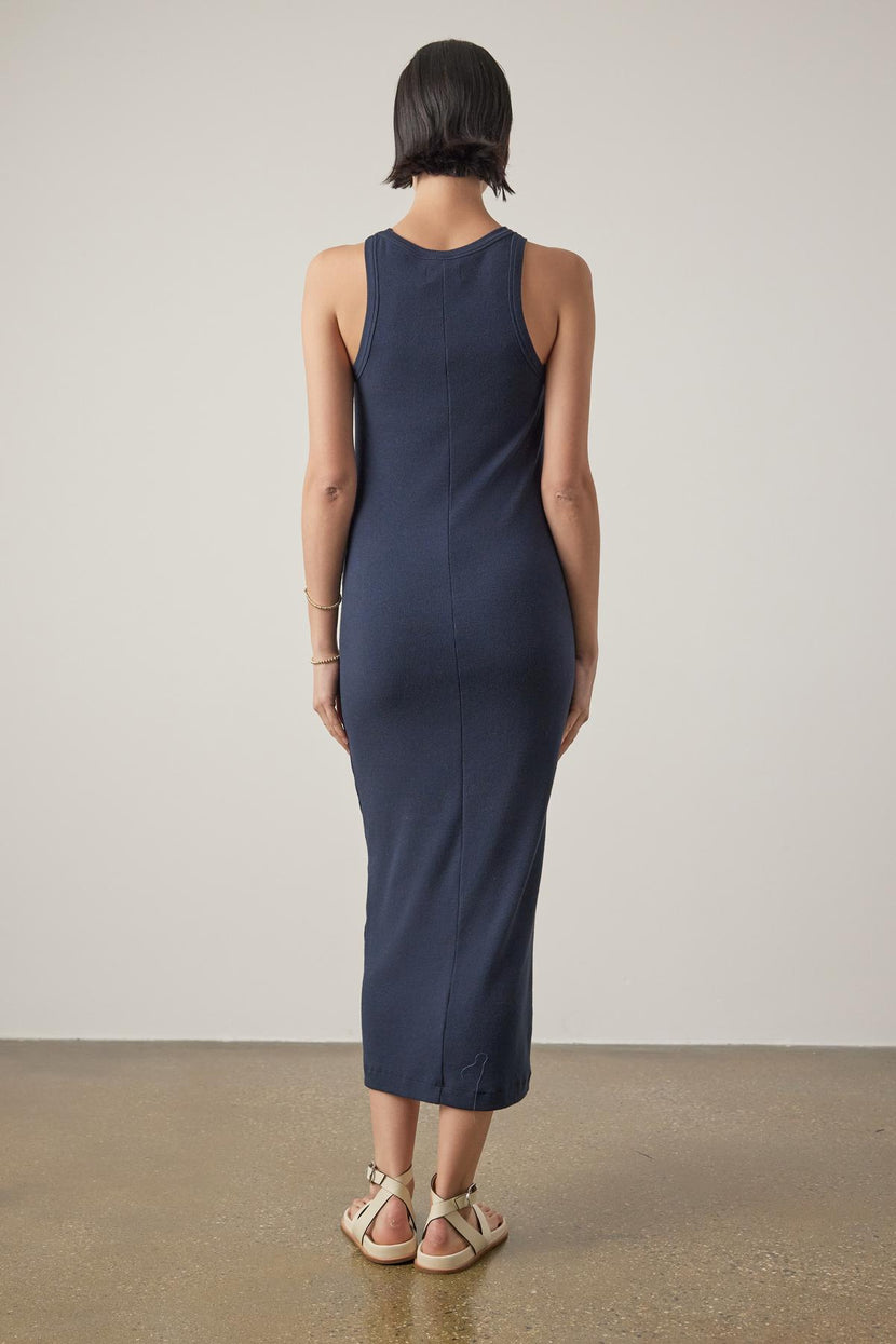 Rear view of a woman in a Navy Blue Velvet by Jenny Graham Griffith Dress with a crew neckline and cream sandals standing against a plain background.