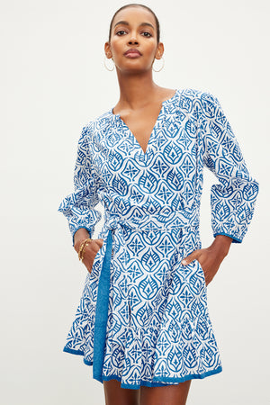 A woman in a KENLEY PRINTED BOHO DRESS by Velvet by Graham & Spencer with a v-neckline and flared sleeves stands confidently against a plain background.