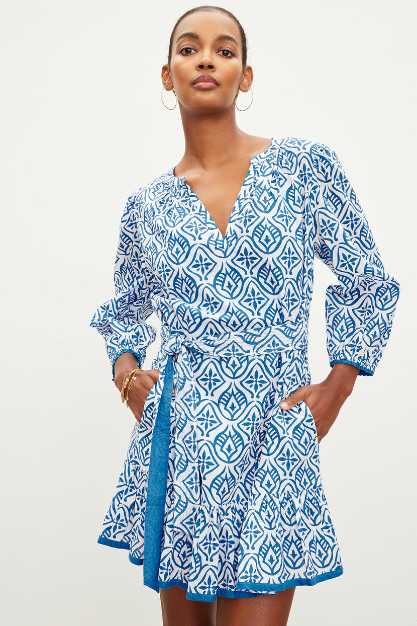 A woman in a KENLEY PRINTED BOHO DRESS by Velvet by Graham & Spencer with a v-neckline and flared sleeves stands confidently against a plain background.
