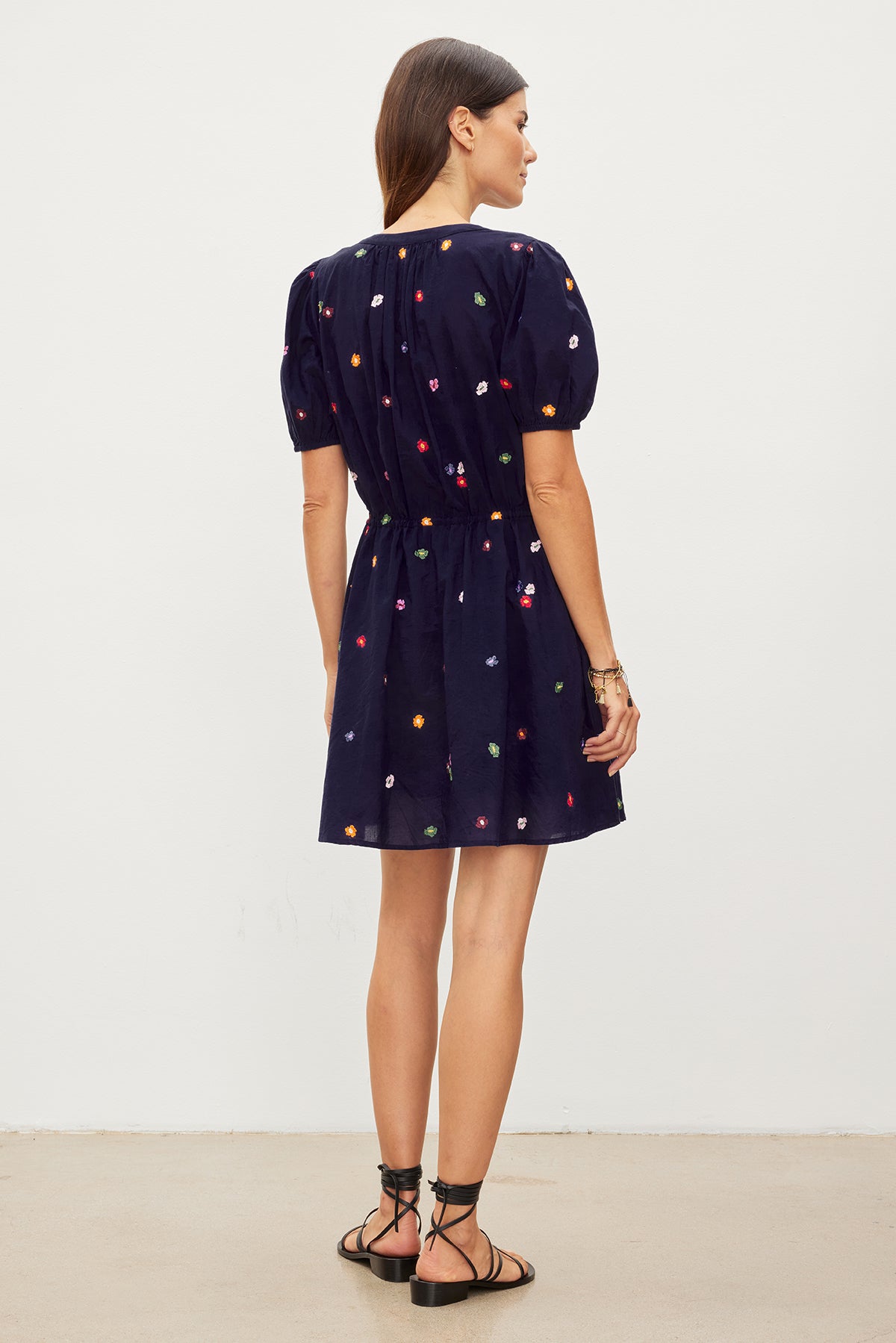   Woman from behind wearing a navy Velvet by Graham & Spencer dress with floral embroidery, tied at the drawstring waist, standing in a neutral setting. 