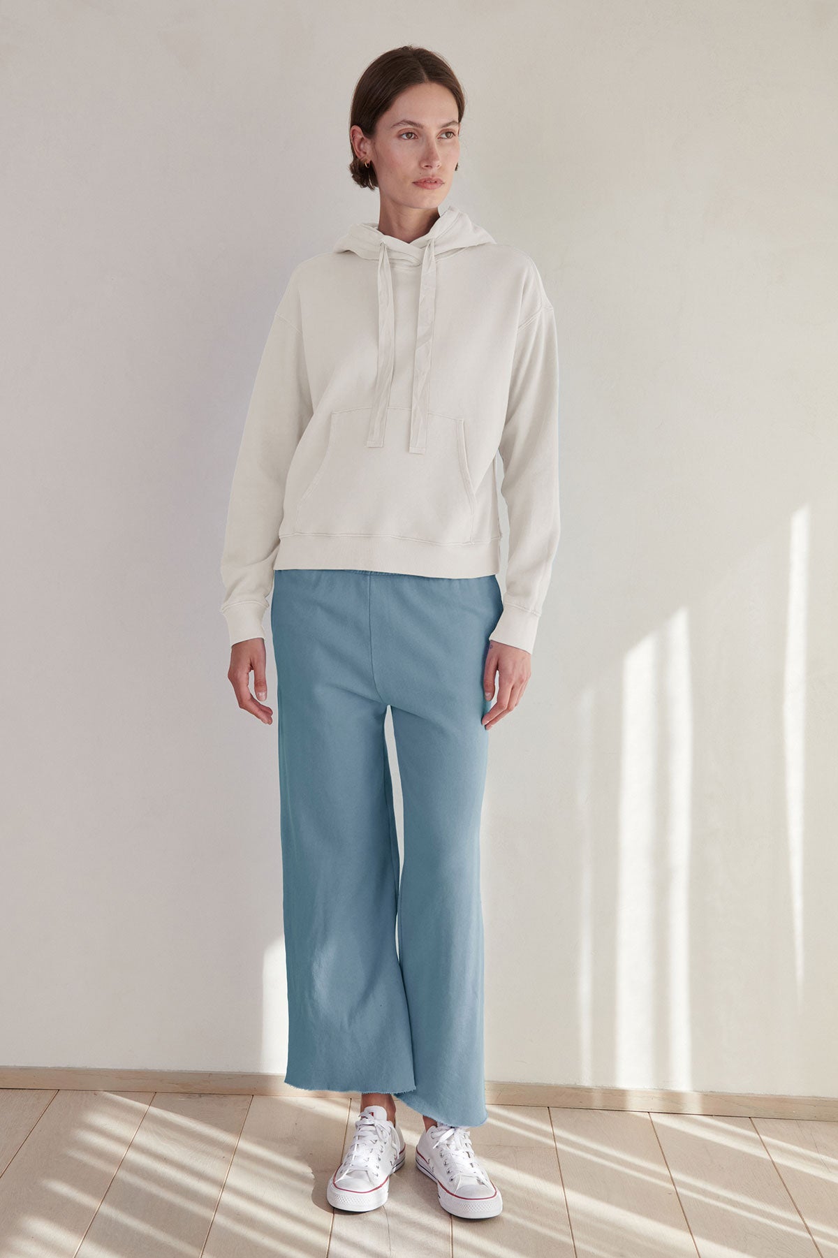 A woman wearing a white hoodie and blue Monetico sweatpant pants by Velvet by Jenny Graham.-36212537786561