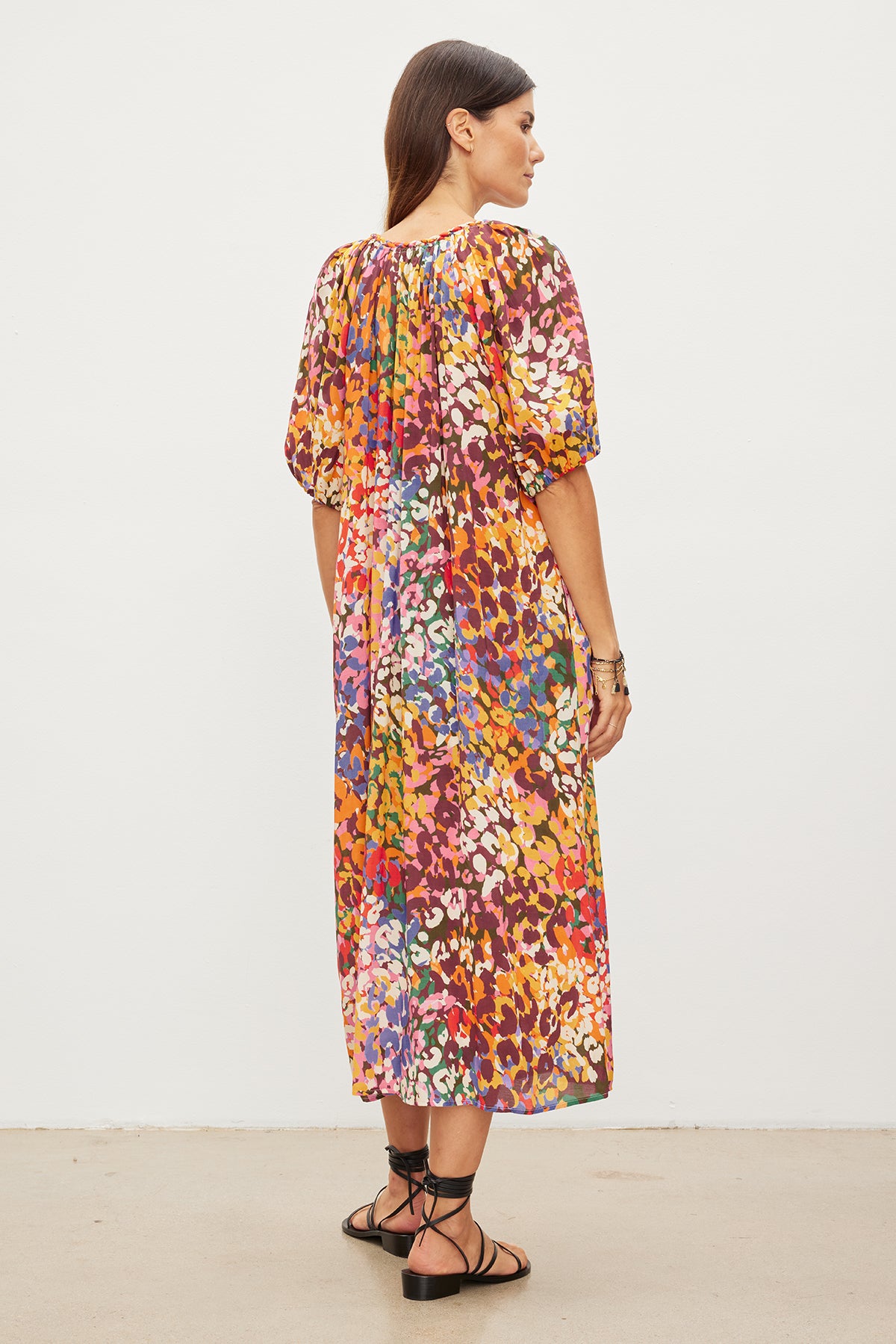 A woman viewed from the side wears a Velvet by Graham & Spencer CAROL PRINTED BOHO DRESS and black strappy sandals, standing against a plain white background.-35955494224065