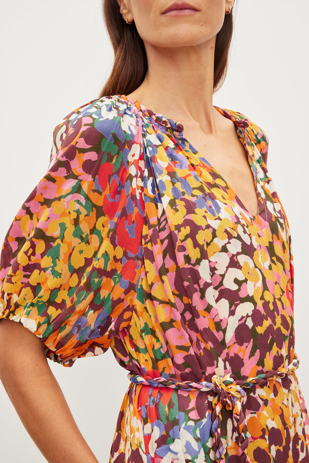   Close-up of a woman wearing a colorful floral printed viscose dress with puff sleeves and a detachable twist braid belt. Only the lower half of her face is visible, in the CAROL PRINTED BOHO DRESS by Velvet by Graham & Spencer. 