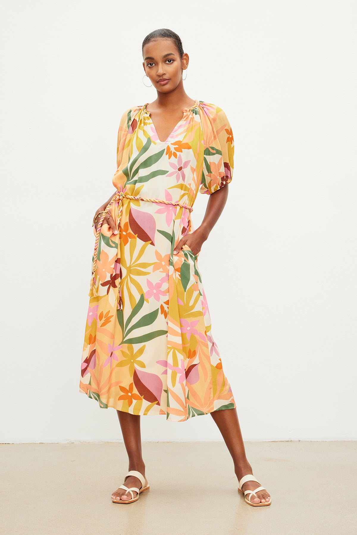 A woman standing, wearing a colorful floral printed CAROL BOHO DRESS by Velvet by Graham & Spencer and beige sandals, with her hands gently resting on her hips.-35955494289601