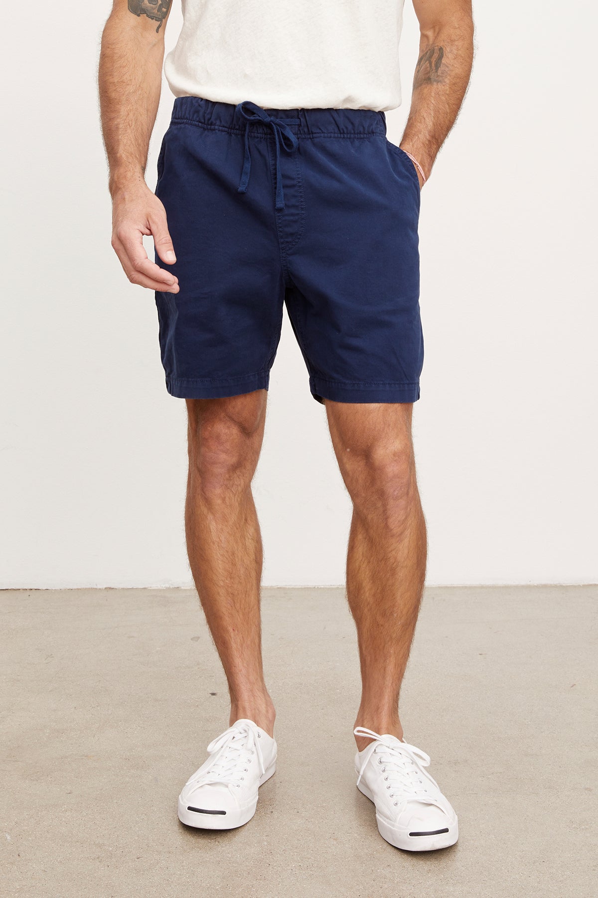 A man wearing navy blue Velvet by Graham & Spencer FIELDER shorts and white sneakers stands against a white background, cropped from the chest down.-36909292323009