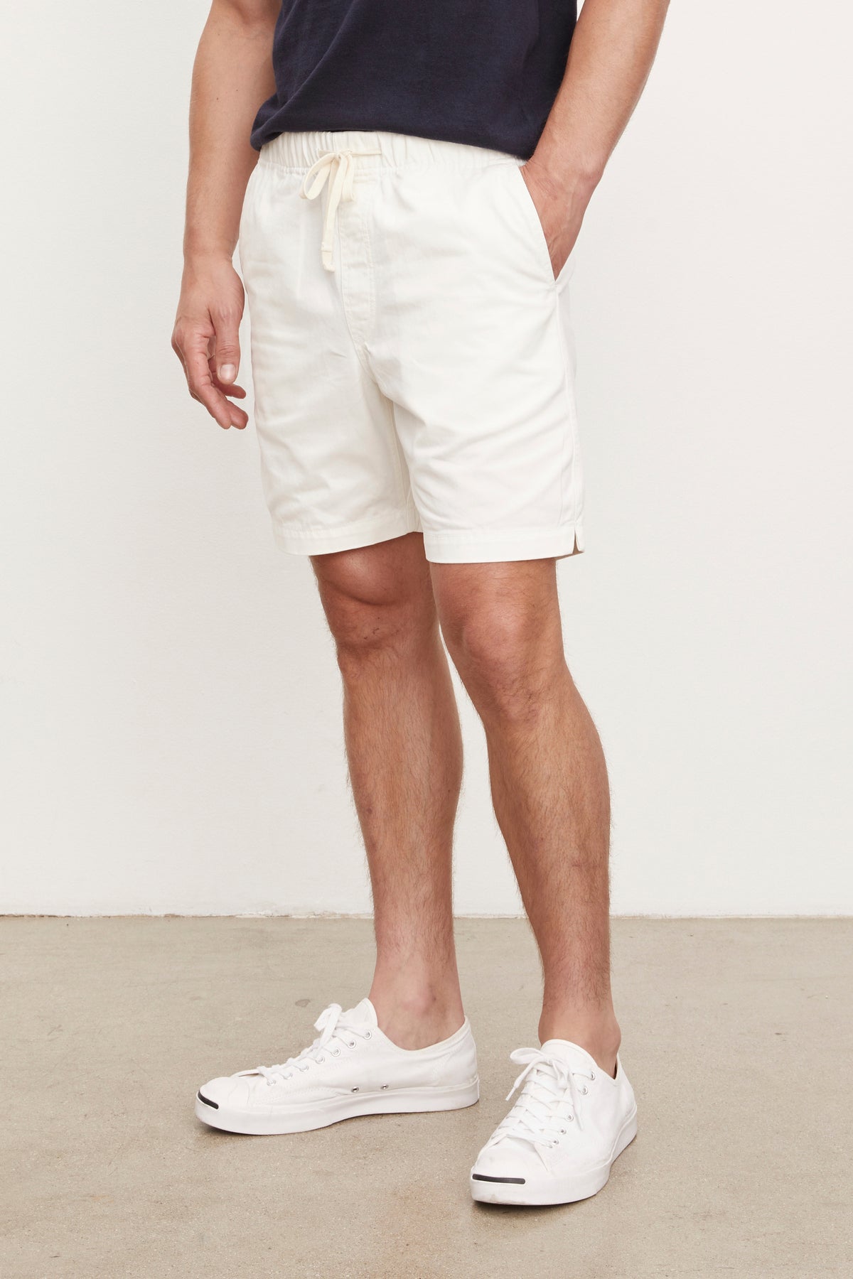 Man wearing a navy blue t-shirt and FIELDER shorts by Velvet by Graham & Spencer with white sneakers, standing in a room with a plain background. Only his torso and legs are visible.-36753575870657