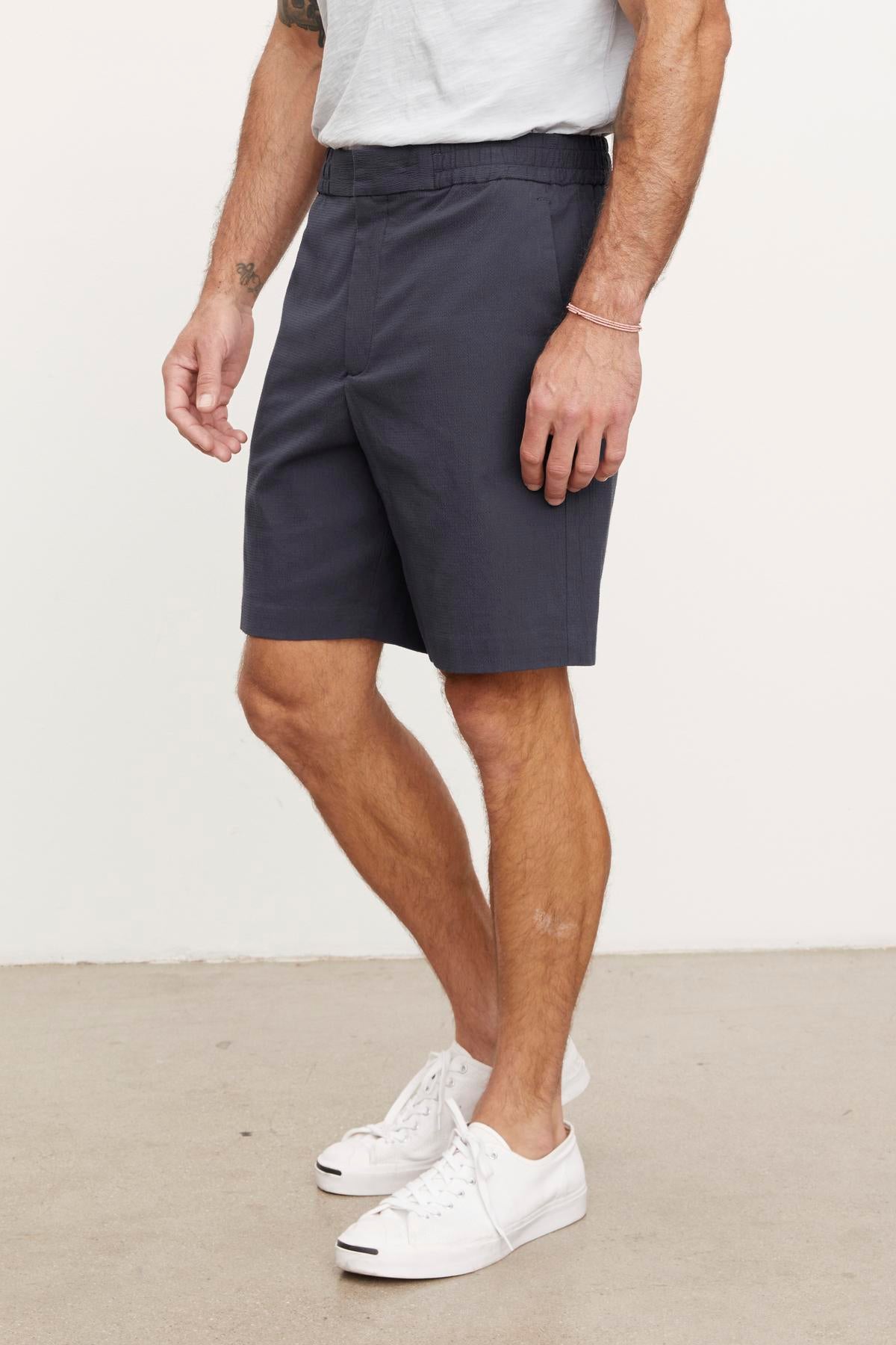 Man standing in a plain background wearing a gray pair of Velvet by Graham & Spencer DAMIAN shorts and white sneakers, showing from waist to shoes.-36890695958721