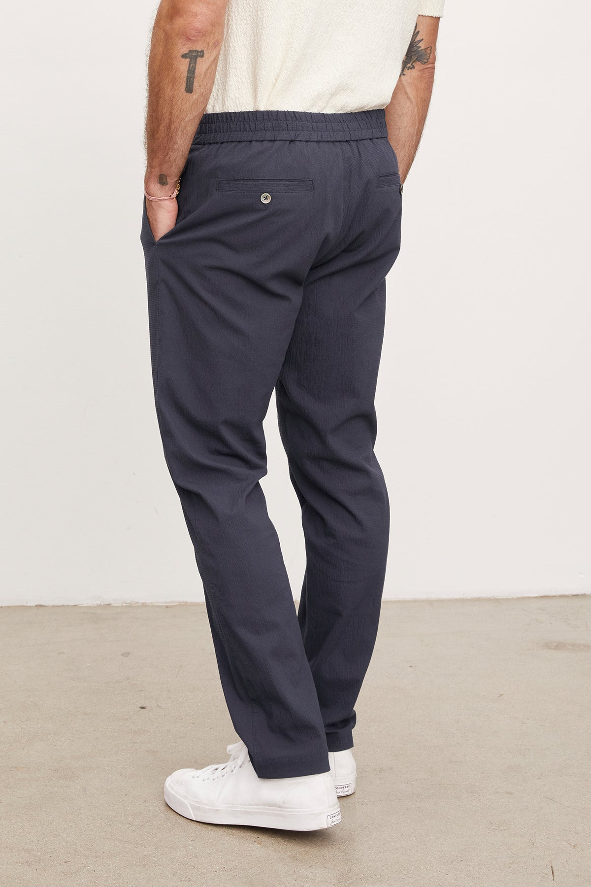 A man wearing dark blue seersucker cotton WILLEM PANTS by Velvet by Graham & Spencer and white sneakers, viewed from the side, focusing on the trouser fit and details.-36909304709313