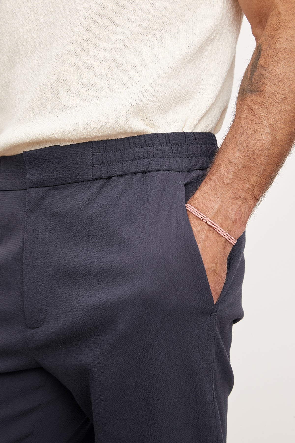 Close-up of a man's side, showing Velvet by Graham & Spencer navy blue seersucker cotton Willem pants with an elastic waistband and a single pocket, against a light beige sweater.-36909304742081