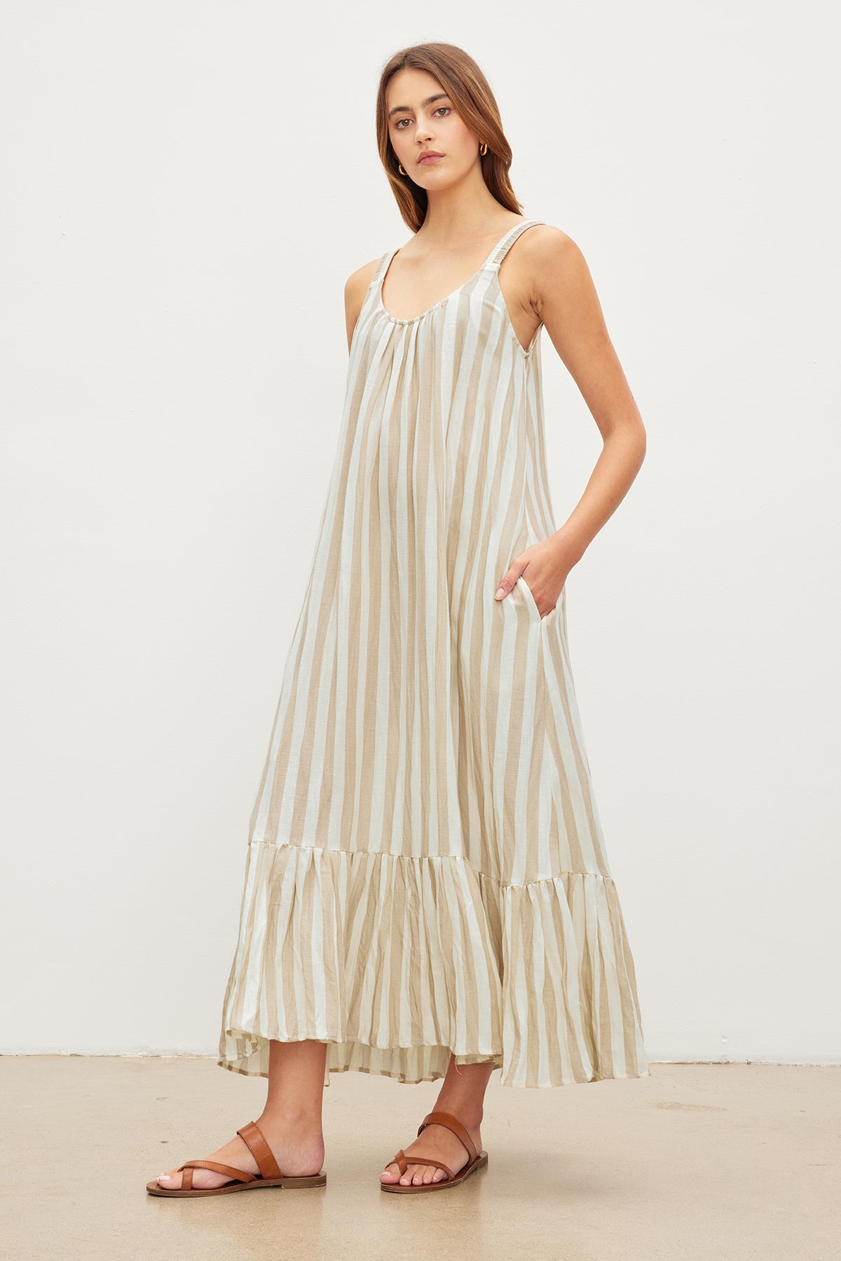   A woman in a MERADITH STRIPED LINEN MAXI DRESS by Velvet by Graham & Spencer and brown sandals standing in a neutral-toned studio. 