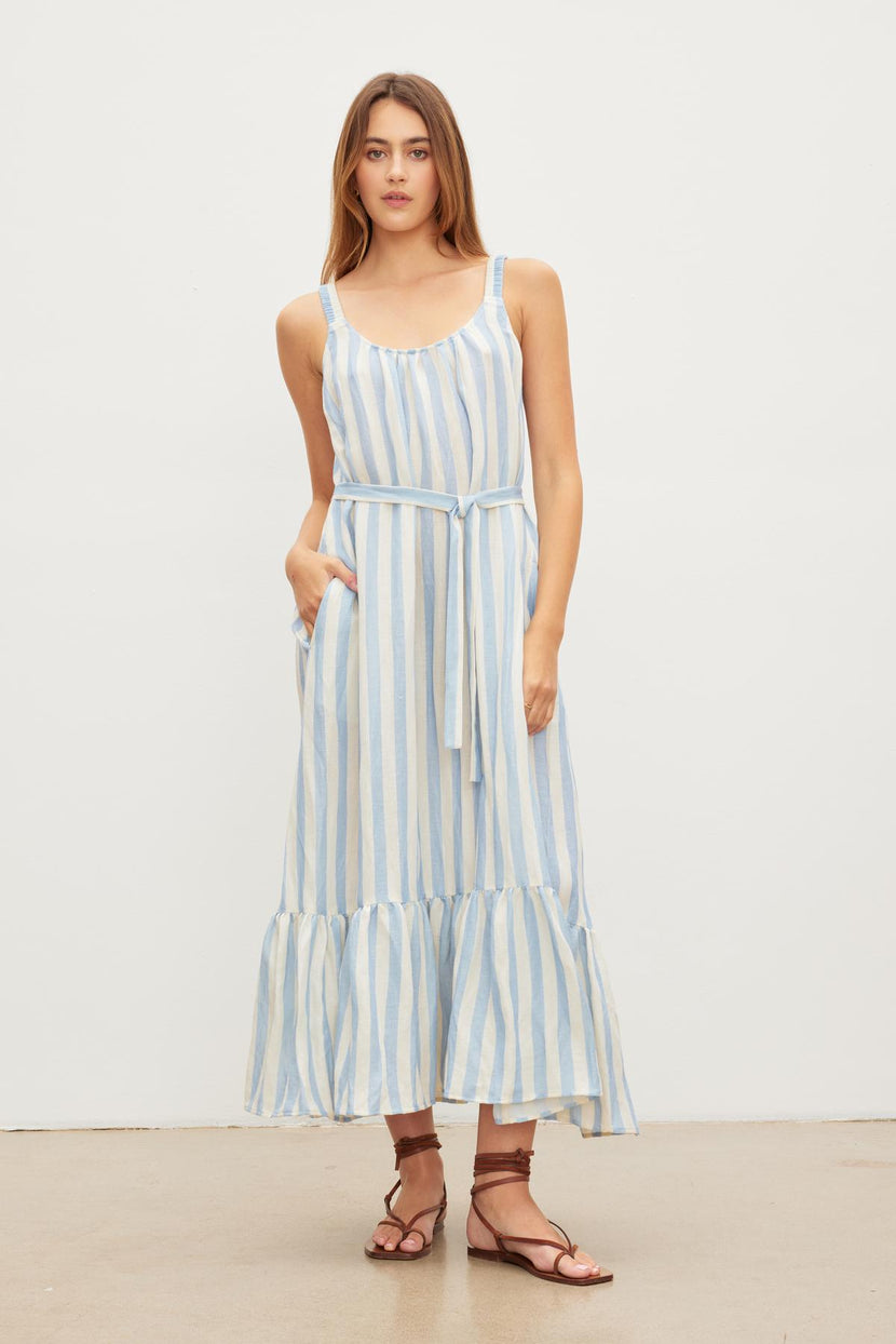 Woman standing against a plain background, wearing a Velvet by Graham & Spencer MERADITH STRIPED LINEN MAXI DRESS with ruffles and sandals.