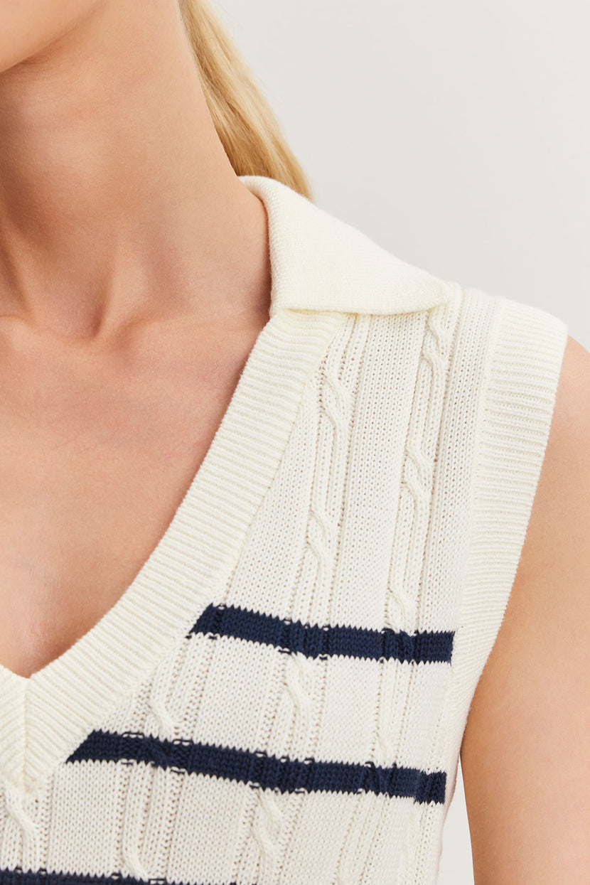 Close-up of a woman wearing a Velvet by Graham & Spencer WENDY SWEATER VEST in cream-colored cable knit with a navy blue stripe detail.