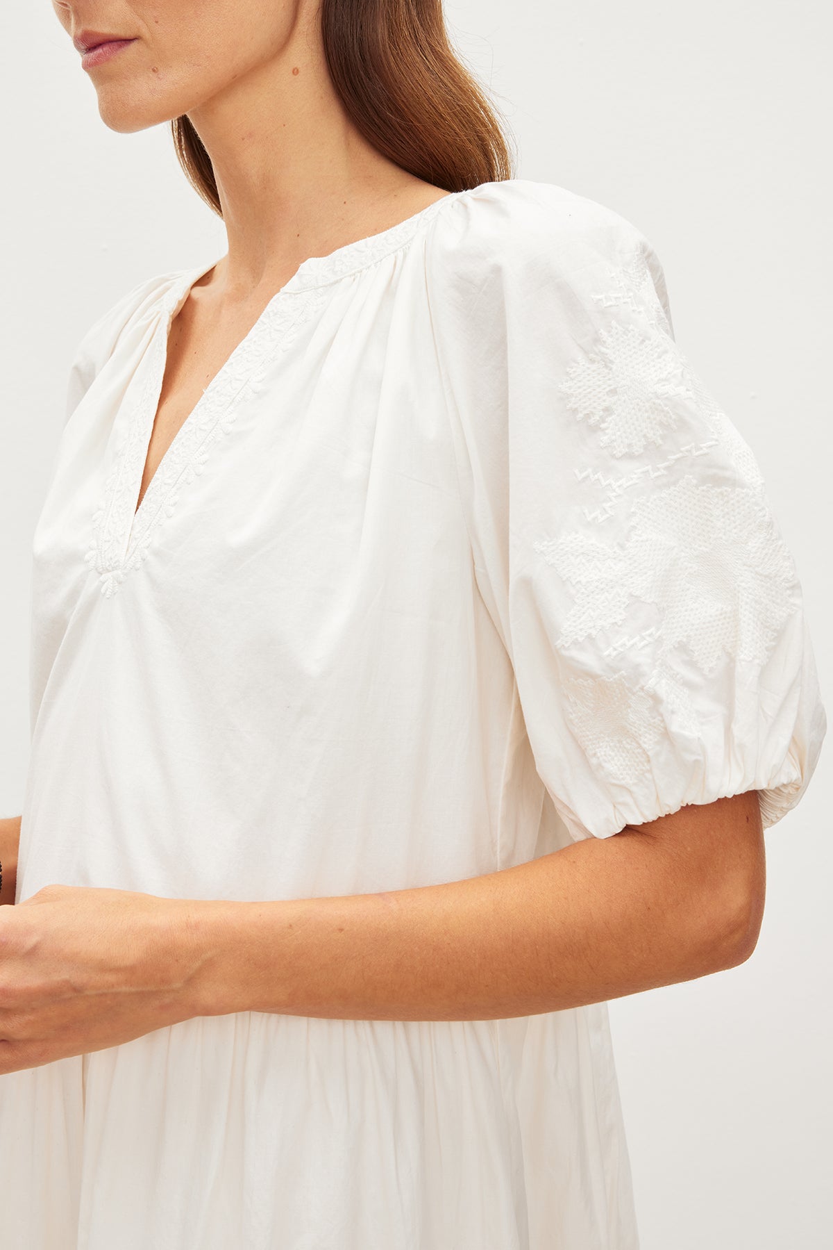   Close-up of a woman in a white cotton dress with floral embroidered puff sleeves, focusing on the shoulder and v-neckline details of the CHRISSY EMBROIDERED BOHO DRESS by Velvet by Graham & Spencer. 