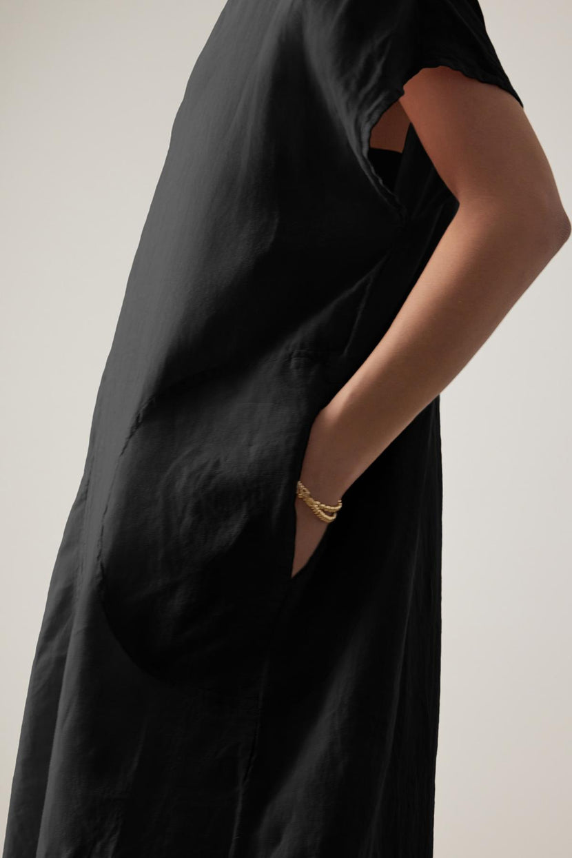 A close-up of a person wearing a Velvet by Jenny Graham black Montana linen dress with a cut-out detail at the elbow and a gold bracelet on the wrist.