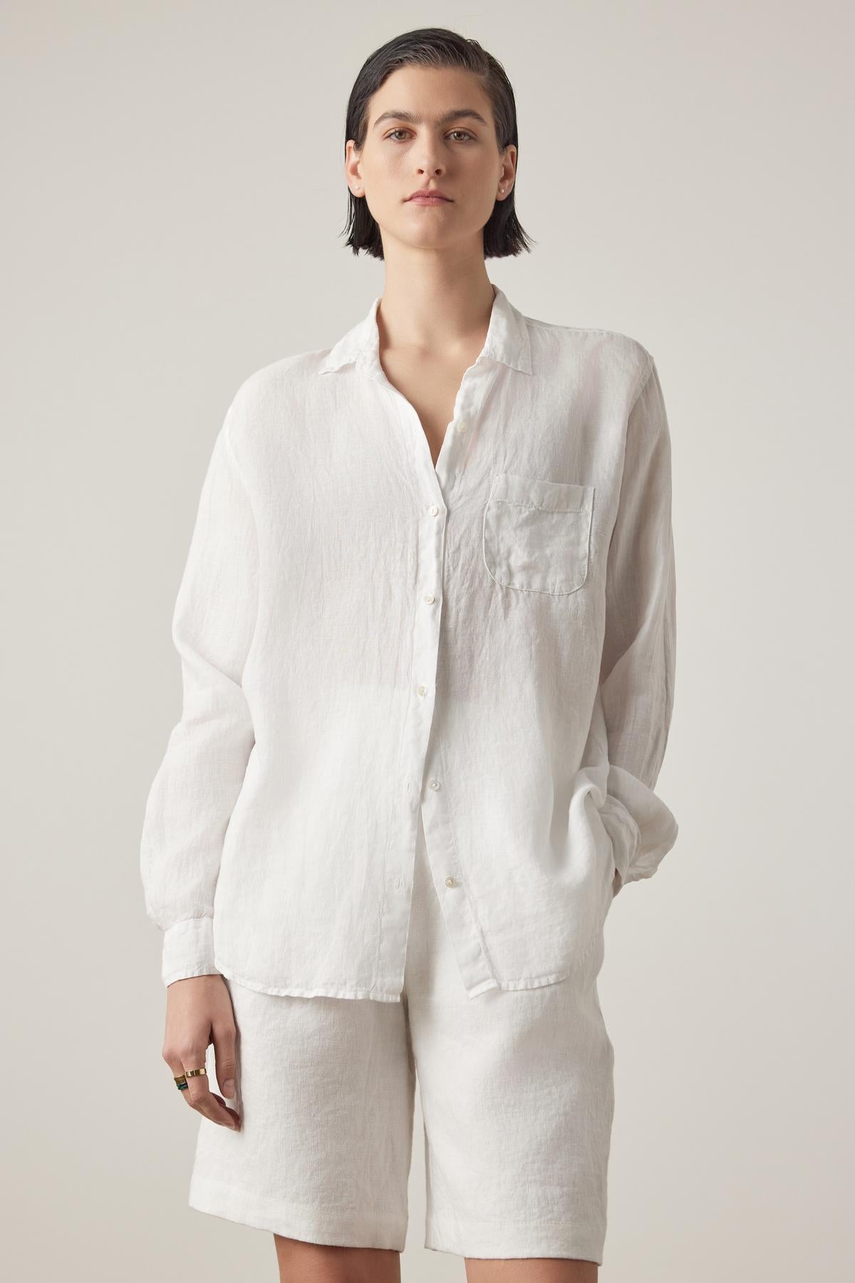 Person with short dark hair wearing a Velvet by Jenny Graham MULHOLLAND LINEN SHIRT with a scooped hemline and matching white shorts, standing against a plain background.-37018505117889