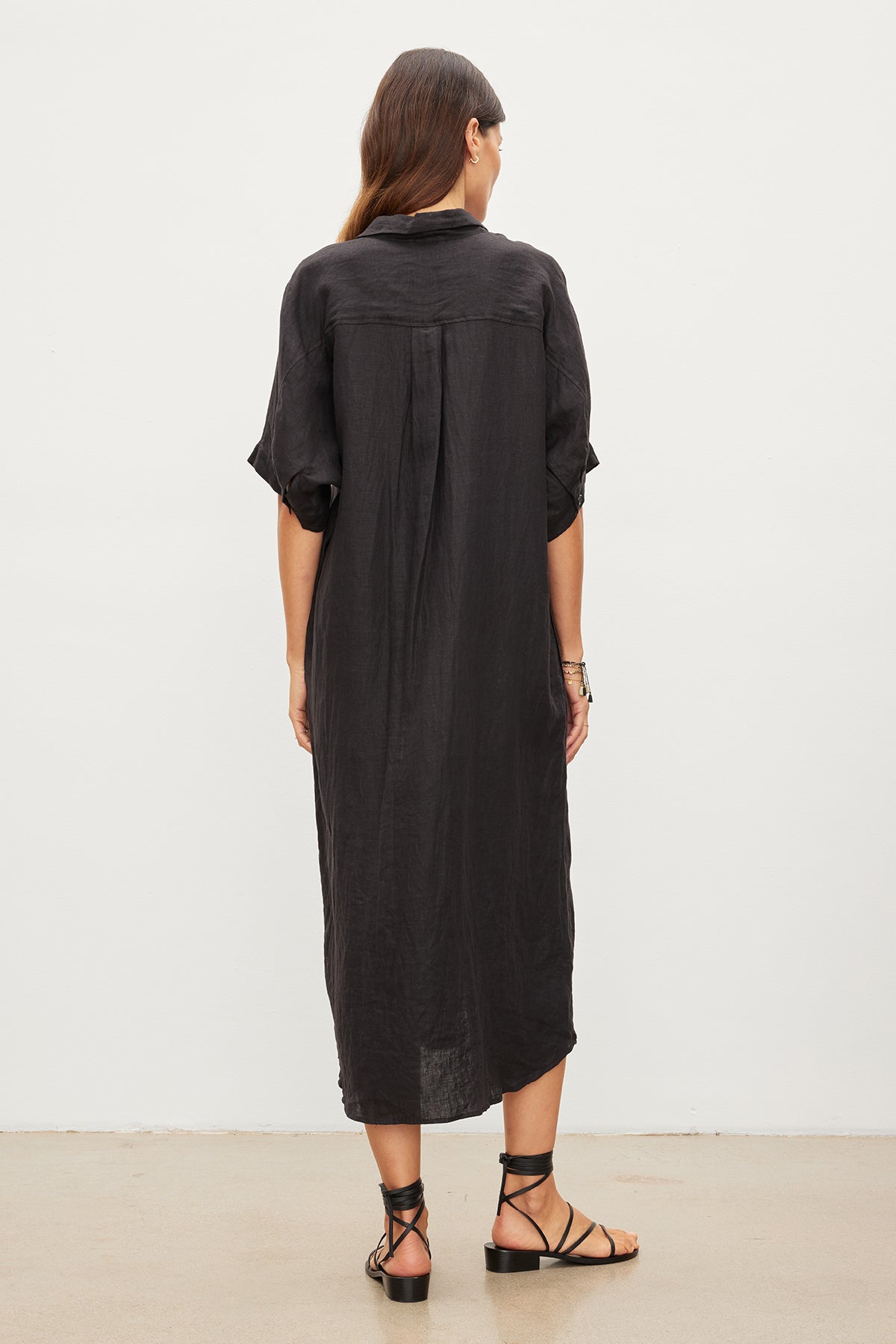 Rear view of a woman wearing a Velvet by Graham & Spencer SANDRA LINEN BUTTON-UP DRESS with short sleeves and sandals, standing against a white background.-35967717638337