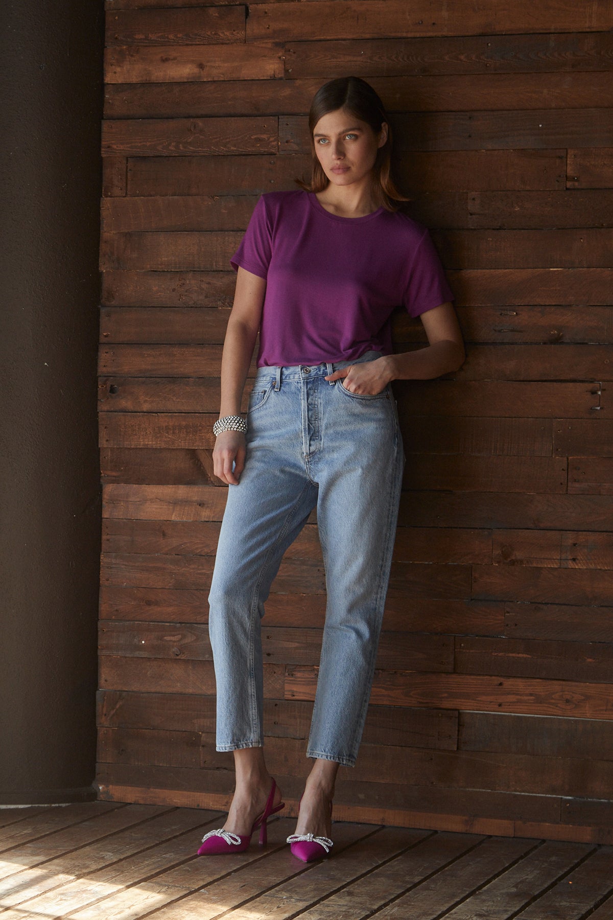 A woman leaning against a wooden wall in a soft Velvet by Jenny Graham SOLANA TEE and jeans.-25483501142209