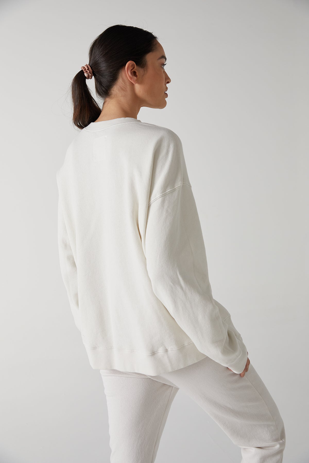 The back view of a woman wearing a Velvet by Jenny Graham ABBOT sweatshirt made of organic cotton and white pants, showcasing the slouch and styling versatility.-25483446157505
