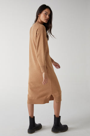 The model is wearing a LAUREL DRESS by Velvet by Jenny Graham, a modern sweater dress with side hem slits, in a camel hue.