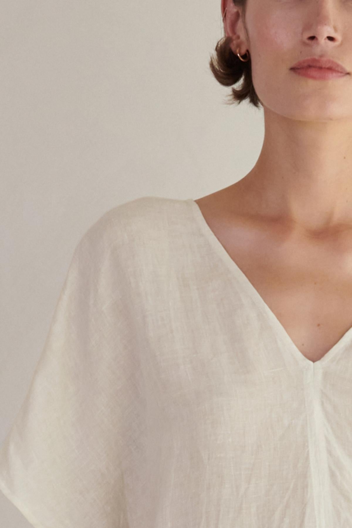 Close-up of a woman in a Montana Linen Dress from Velvet by Jenny Graham, focusing on the V neckline and shoulder area, with a soft-focus background.-26293194981569